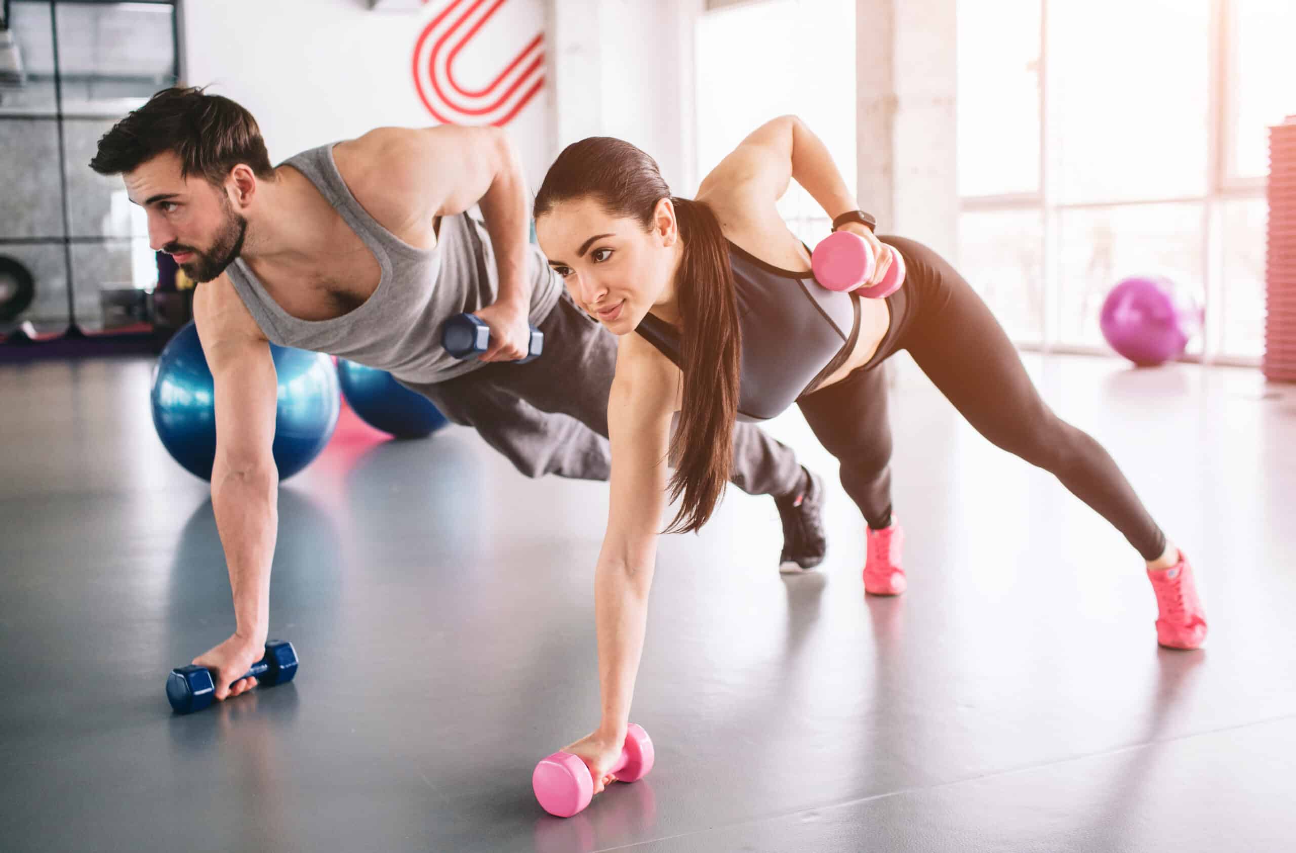 Homme et femme musclés faisant une planche haltères en salle de sport, concentrés sur leur entraînement