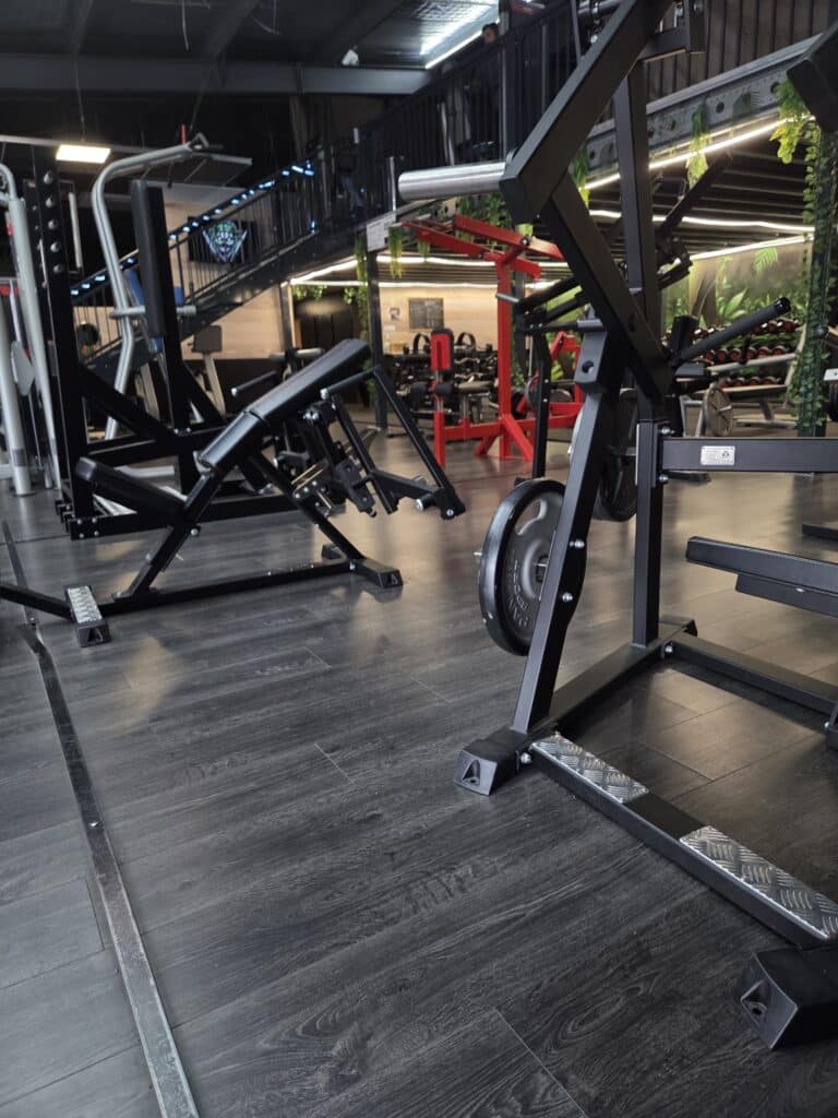 Salle de Sport Moderne: Équipements Noirs et Rouges Intérieur d'une salle de sport moderne avec sol foncé, machines noires et rouges, escalier avec éclairage bleu et décorations végétales.